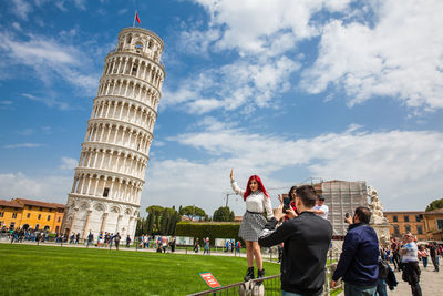 Group of people in front of building against cloudy sky