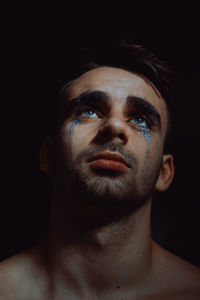 Close-up of man with glitter on face against black background