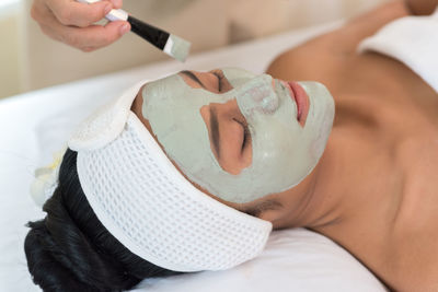 Cropped hands of beautician applying facial mask on woman face at spa