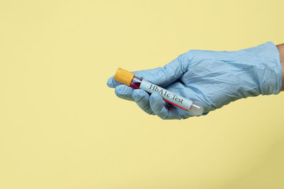 Low section of person holding umbrella against yellow wall