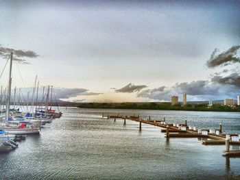 Boats moored in calm sea against cloudy sky