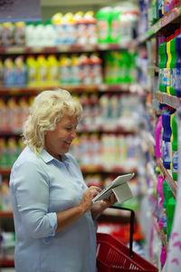 Side view of smiling senior woman using digital tablet while shopping in supermarket