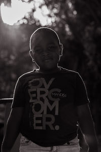 Portrait of cute boy standing outdoors against sunbeams