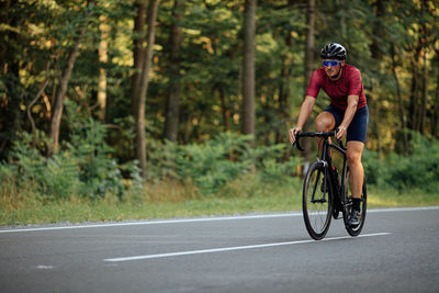 Muscular young guy wearing protective helmet, mirrored glases and sport outfit riding black bike