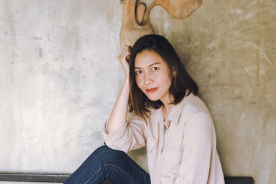 Portrait of a beautiful young woman sitting against wall