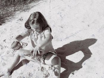 High angle view of girl playing with sand while sitting on beach during sunny day
