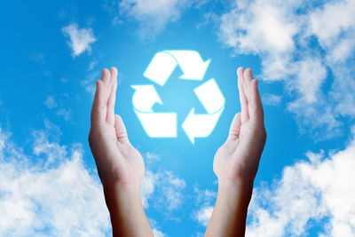 Cropped hands with recycling symbol against cloudy sky