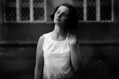 Thoughtful young woman with eyes closed standing against wall