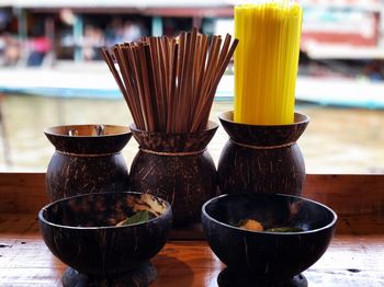 Close-up of wooden bowl with chopsticks and drinking straws on table