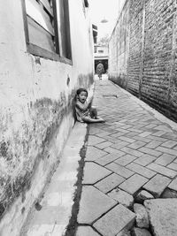 Man sitting on footpath against wall