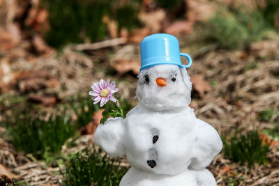 Snowman standing on grass with flower in his hand