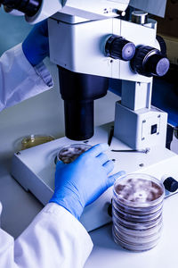 Cropped hands of scientist holding petri dish on microscope