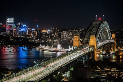 Illuminated bridge over river amidst buildings in city at night