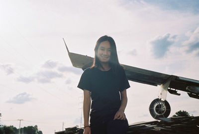 Portrait of woman standing by airplane against sky