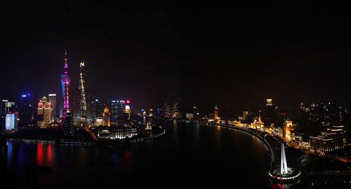 Illuminated buildings by river against sky at night