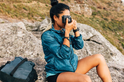 Woman photographing while sitting on rock