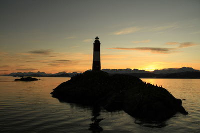 Silhouette lighthouse by sea against sky during sunset