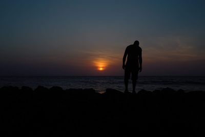 Silhouette man standing on rock at beach against sky