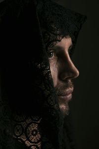 Close-up of man with lace covering head against black background
