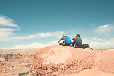 Rear view of man sitting on mountain against cloudy sky