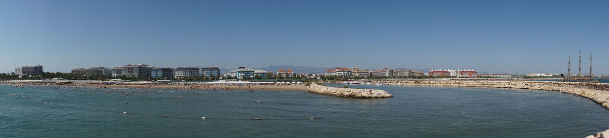 Sailboats in sea by city against clear blue sky