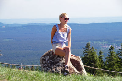 Full length of woman sitting on rock against landscape