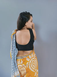 Woman looking away while standing against gray background