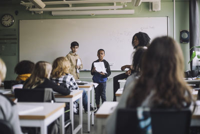 Boys holding reports while doing presentation to students in classroom