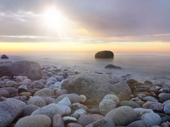 Rocks on beach against sky during sunset