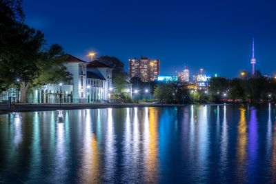 Illuminated buildings by lake against blue sky at night