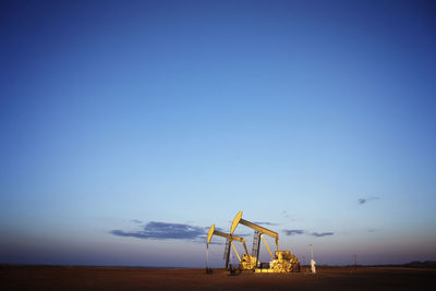 Oil pumps on field against blue sky