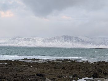 Scenic view of sea by snowcapped mountains against sky