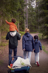 Rear view of family walking on trail amidst trees in forest