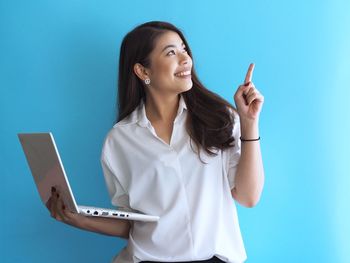 Young woman using phone while standing against blue background