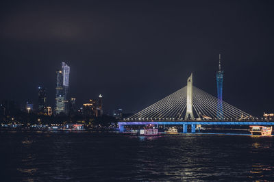 Illuminated bridge over river against buildings at night