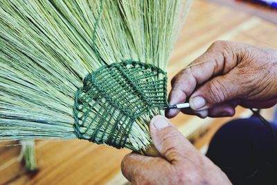 Close-up of cropped hand sewing brooms at workshop