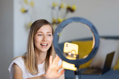 Young woman making photo or video content for social media with smartphone and light of ring lamp