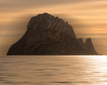 Rock formation in sea against sky during sunset