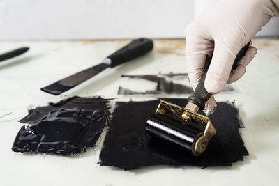 Closeup hand of crop anonymous artisan in glove using braver and spreading ink on sheet for engraving while working in professional workshop