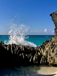 Sea waves splashing on rocks against blue sky