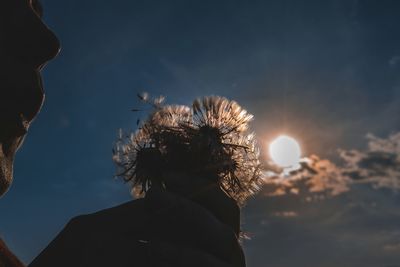 Close-up of man blowing dandelion against sky