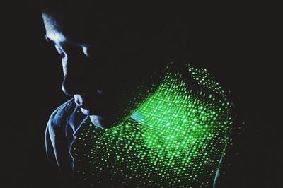 Close-up of shirtless woman with illuminated green lights against black background