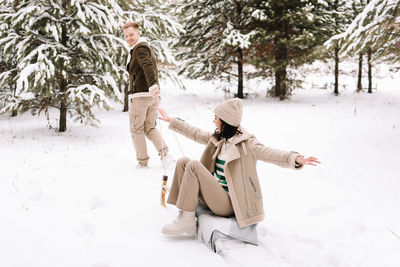 A man and a woman in love have fun and ride sleigh in the forest among the trees in winter in nature