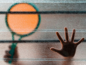 Close-up of a boy's hand holding a badminton racquet behing a textured glass window