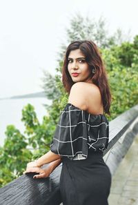 Portrait of beautiful young woman standing against sky