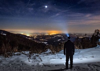 Rear view of man standing on snow against sky at night