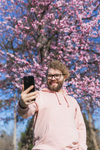 Young woman photographing with mobile phone while standing against trees