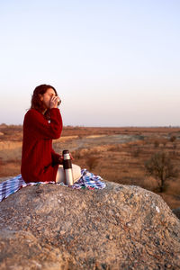 Young happy woman in red sweather relaxing, drinking coffee and enjoying sunset in autumn. person