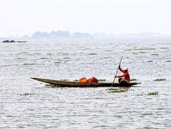 Man rowing boat in sea against sky