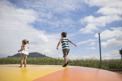 Rear view of boy and girl jumping on large trampoline outdoors.